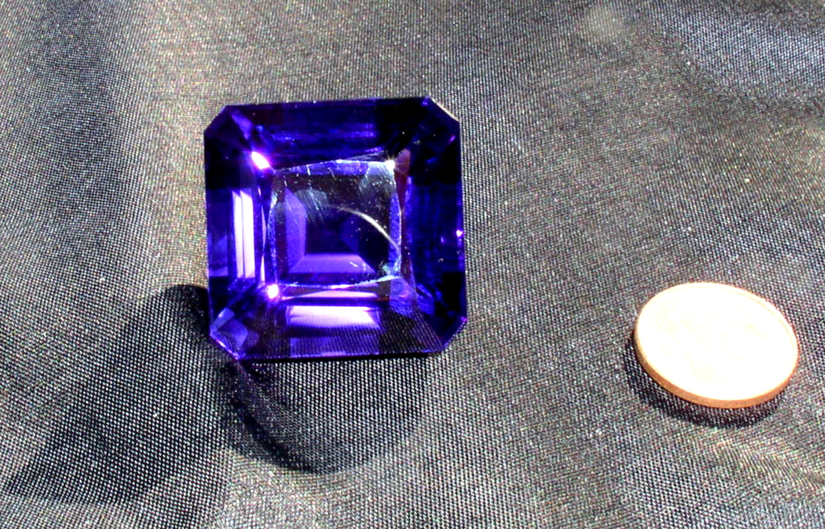 Large faceted purple amethyst beside a coin showing its size
