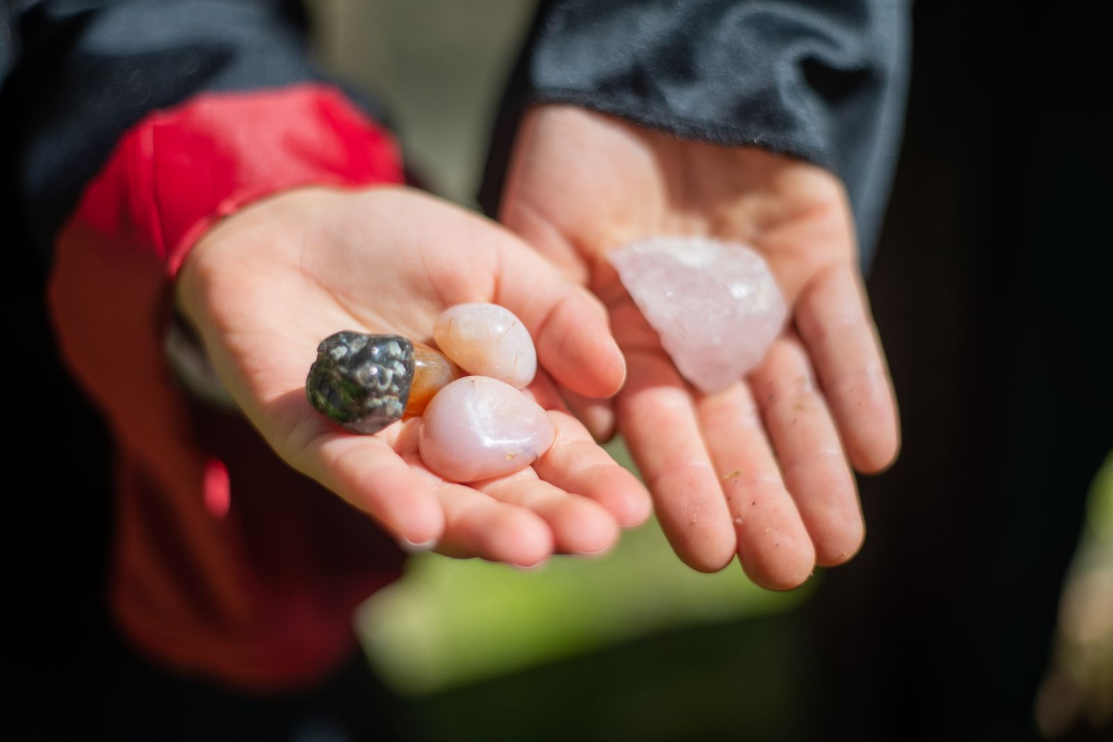 Hands holding tumbled gemstones including rose quartz